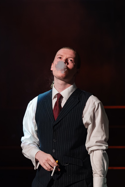 Edward Wenborn as Nick Shadow using a Stage Props theatrical cigarette in British Youth Opera’s 1980s-set production of The Rake’s Progress.